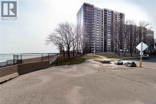 High-rise building featuring multiple balconies and a brick facade, set on a landscaped embankment with mature trees - 500 Green Road Unit# 901, Stoney Creek, ON - Outdoor