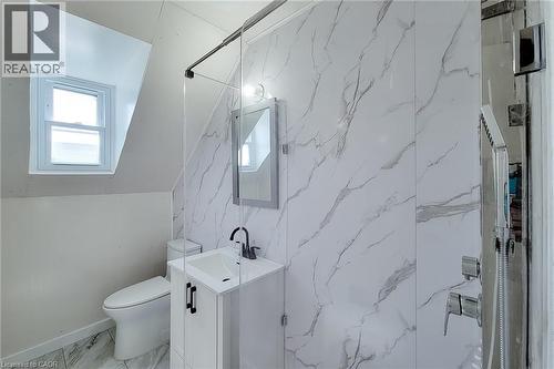 Bathroom featuring marble-patterned wall panels, a white vanity with black hardware, a modern toilet, and a glass-enclosed shower with a handheld showerhead - 78 Hillyard Street, Hamilton, ON - Indoor Photo Showing Bathroom