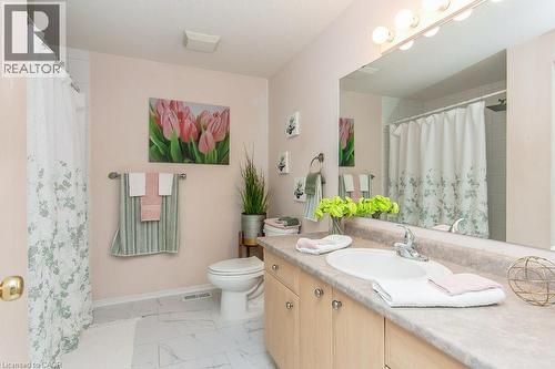 Bathroom featuring a single vanity with an integrated sink, broad wall mirror, vanity lighting fixture, wood-finish cabinetry, and a shower-tub combination - 71 Foxglove Crescent, Kitchener, ON - Indoor Photo Showing Bathroom