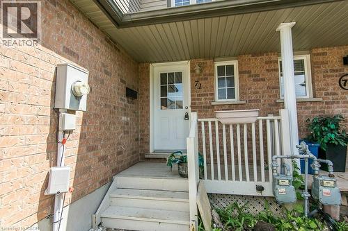 Brick exterior facade with a white entry door featuring glass panels, an exterior light fixture, and a white wood-finish porch with railings and steps - 71 Foxglove Crescent, Kitchener, ON - Outdoor With Deck Patio Veranda With Exterior