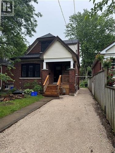 Brick exterior with white siding accents and a covered front porch featuring wooden steps - 21 Haddon Avenue S, Hamilton, ON 