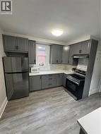 Modern kitchen featuring gray shaker cabinetry, light countertops, subway tile backsplash, stainless steel appliances, and wood-finish flooring - 