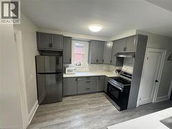 Modern kitchen featuring gray cabinetry with matte black hardware, stainless steel appliances, white countertops, and a white subway tile backsplash - 