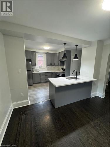 Modern kitchen featuring grey cabinetry, stainless steel appliances, and a central island with a sink - 21 Haddon Avenue S, Hamilton, ON 