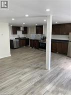 Spacious kitchen area featuring wood-finish flooring, recessed lighting, dark wood cabinetry, stainless steel appliances, and dark countertops - 
