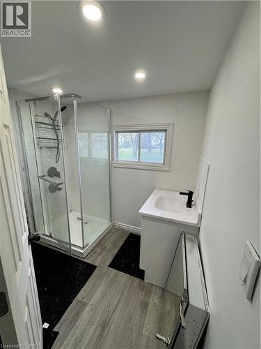 Bathroom featuring a glass-enclosed shower with subway tile surround, a single vanity with an integrated sink and black faucet, recessed ceiling lighting, and wood-finish flooring - 28 Derner Line, Lowbanks, ON - Indoor Photo Showing Bathroom