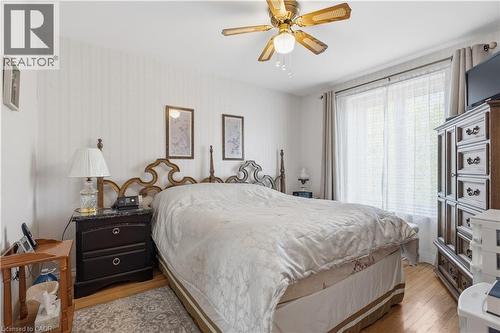 Bedroom featuring hardwood flooring, a ceiling fan with integrated lighting, a large window with sheer and blackout curtains, and textured wallpaper - 1526 Westminster Place, Burlington, ON - Indoor Photo Showing Bedroom