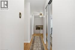 Hallway featuring wood-finish flooring, white baseboards, and a ceiling fan with integrated lighting - 