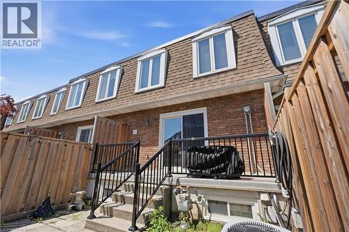 Brick exterior with a mansard roof, featuring multiple dormer windows, a sliding glass door, and a private wooden fence - 1526 Westminster Place, Burlington, ON - Outdoor With Exterior