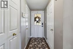 Entryway featuring a white paneled door with glass insert, wood-finish flooring, and multiple white paneled closet doors with brass hardware - 