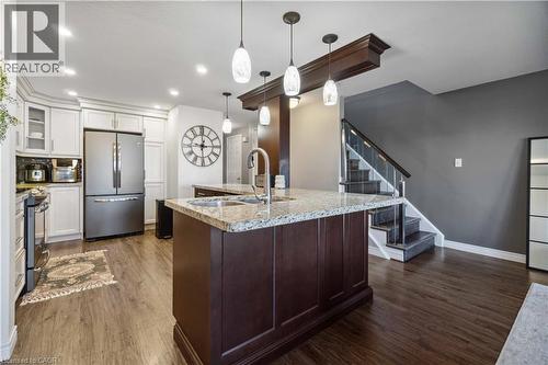 Kitchen featuring a large island with a stainless steel sink, light-toned granite countertops, wood-finish flooring, white cabinetry, and stainless steel appliances - 27 Red Clover Crescent, Kitchener, ON - Indoor Photo Showing Kitchen With Stainless Steel Kitchen With Upgraded Kitchen