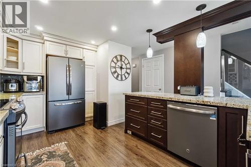 Kitchen featuring wood-finish flooring, recessed lighting, white perimeter cabinetry with crown molding, a stainless-steel refrigerator, and an island with dark wood cabinetry and a light-toned counte - 27 Red Clover Crescent, Kitchener, ON - Indoor Photo Showing Kitchen With Stainless Steel Kitchen With Upgraded Kitchen