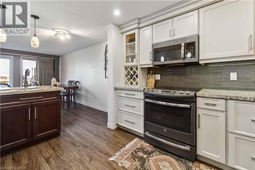 Kitchen featuring wood-finish flooring, two-tone cabinetry, stainless steel appliances, a tile backsplash, and stone countertops - 27 Red Clover Crescent, Kitchener, ON - Indoor Photo Showing Kitchen