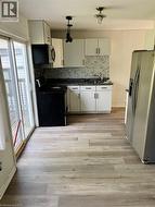 Kitchen featuring wood-finish flooring, white cabinetry, dark countertops, a tiled backsplash, and stainless steel appliances - 