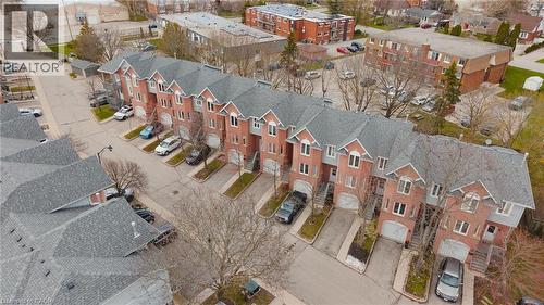 Row of townhomes featuring red brick facades, multiple gabled roofs with dark shingles, individual garage entrances, and paved driveways - 245 Bishop Street S Unit# 31, Cambridge, ON - 