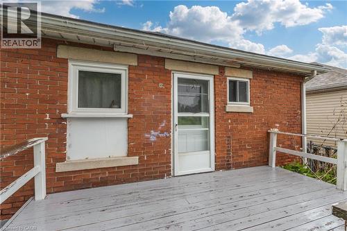 Brick exterior featuring a wooden deck with railing, white framed windows, and a white framed entry door with screen - 46 East 16Th Street, Hamilton, ON - Outdoor With Exterior