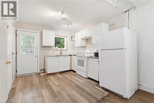 Kitchen featuring wood-finish flooring, white cabinetry, a sink with a window, white appliances, and a rear exterior door with a glass insert - 46 East 16Th Street, Hamilton, ON - Indoor Photo Showing Kitchen