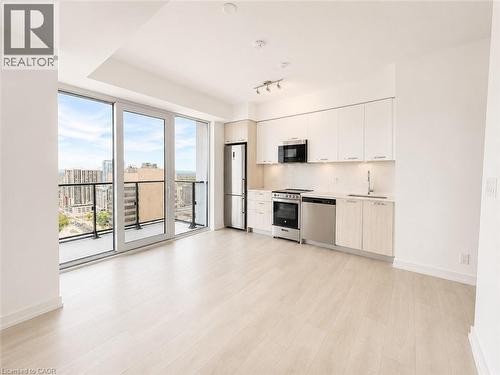 Open-concept living area with wood-finish flooring, a contemporary kitchen featuring stainless steel appliances and white cabinetry, and a private balcony with glass railing - 75 James Street S Unit# 2614, Hamilton, ON - Indoor Photo Showing Kitchen