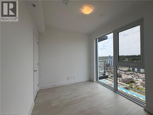 Spacious room with wood-finish flooring, a contemporary ceiling light fixture, and large windows offering urban and natural scenery - 75 James Street S Unit# 2614, Hamilton, ON - Indoor Photo Showing Other Room