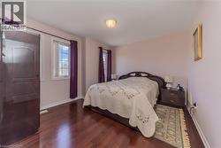 Spacious bedroom featuring rich wood-finish flooring, light-toned walls, and multiple windows - 