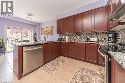 Kitchen featuring rich wood-finish cabinetry, granite countertops, and a mosaic tile backsplash - 675 Best Road, Milton, ON - Indoor Photo Showing Kitchen With Double Sink