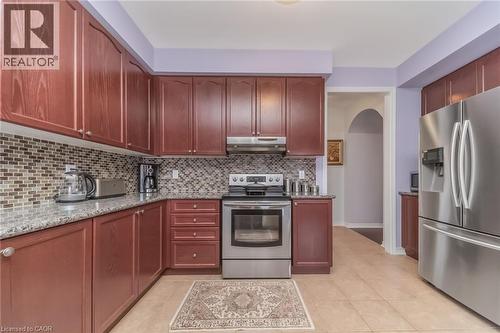 Kitchen featuring extensive wood-finish cabinetry, stainless steel appliances, a mosaic tile backsplash, and light-toned tile flooring - 675 Best Road, Milton, ON - Indoor Photo Showing Kitchen