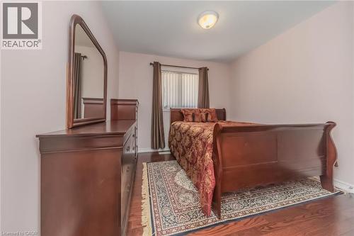 Hardwood flooring throughout featuring a window with vertical blinds and dark curtains, and an overhead flush-mount light fixture - 675 Best Road, Milton, ON - Indoor Photo Showing Bedroom
