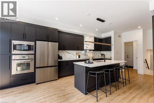 Contemporary kitchen featuring dark flat-panel cabinetry, stainless steel appliances, a center island with seating, and wood-finish flooring - 916 Steepleridge Court, Kitchener, ON - Indoor Photo Showing Kitchen With Stainless Steel Kitchen