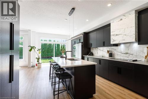 Modern kitchen featuring a large center island with seating, dark wood-finish cabinetry, light wood-finish flooring, a white countertop, and a white marble-patterned backsplash - 916 Steepleridge Court, Kitchener, ON - Indoor Photo Showing Kitchen With Double Sink With Upgraded Kitchen