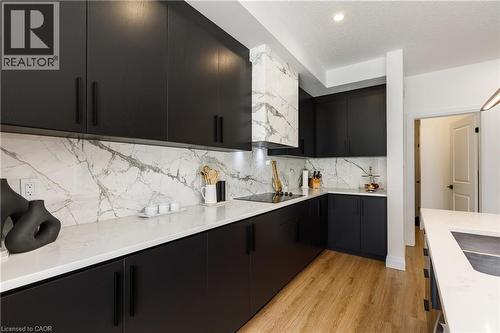 Sleek kitchen featuring dark-finish cabinetry, light-toned countertops, and a full-height marble-patterned backsplash - 916 Steepleridge Court, Kitchener, ON - Indoor Photo Showing Kitchen With Upgraded Kitchen