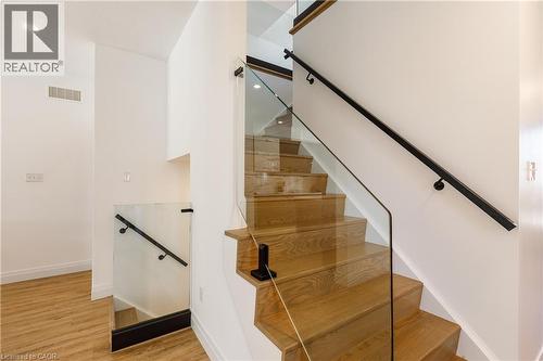 Modern staircase featuring clear glass railings, light wood-finish treads, and a matte black handrail - 916 Steepleridge Court, Kitchener, ON - Indoor Photo Showing Other Room