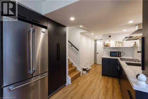 Contemporary kitchen featuring stainless steel appliances, dark flat-panel cabinetry, light wood-finish flooring, recessed lighting, and a white tile backsplash - 916 Steepleridge Court, Kitchener, ON - Indoor Photo Showing Kitchen With Stainless Steel Kitchen