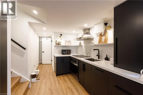 Contemporary kitchen featuring dark flat-panel cabinetry, light stone-finish countertops, a stainless steel range hood, and a matte black faucet - 916 Steepleridge Court, Kitchener, ON - Indoor Photo Showing Kitchen