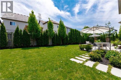 Expansive backyard featuring a manicured lawn, a large patio with a dining area, and concrete stepping stones - 916 Steepleridge Court, Kitchener, ON - Outdoor