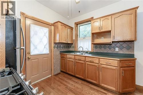 Kitchen featuring wood-finish flooring, natural wood cabinetry, dark countertops, a tile backsplash, and a double basin sink beneath a window - 252 Beechwood Avenue, Hamilton, ON - Indoor Photo Showing Kitchen With Double Sink
