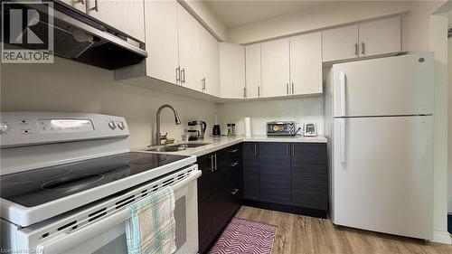 Efficient kitchen featuring white appliances, two-tone cabinetry with light upper and dark lower units, a double basin stainless steel sink with a high-arc faucet, and wood-finish flooring - 206 Indian Road, Kitchener, ON - Indoor Photo Showing Kitchen With Double Sink