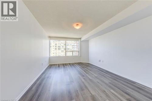 Spacious interior featuring wood-finish flooring, a large window, white walls, and a ceiling-mounted light fixture - 1270 Maple Crossing Boulevard Unit# 1705, Burlington, ON - Indoor Photo Showing Other Room