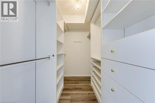 Walk-in closet featuring custom white cabinetry, multiple shelves, integrated drawers with gold-toned hardware, and wood-finish flooring - 1270 Maple Crossing Boulevard Unit# 1705, Burlington, ON - Indoor Photo Showing Other Room