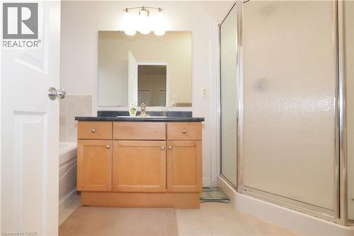 En suite bathroom featuring a light wood-finish vanity with a dark countertop, a large mirror, a separate   glass shower and large deep soaker tub. - 565 Springwater Drive, Waterloo, ON - Indoor Photo Showing Bathroom
