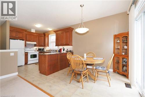 Kitchen and dining area featuring warm wood cabinetry, a peninsula,  white appliances, and light-toned tile flooring - 565 Springwater Drive, Waterloo, ON - Indoor