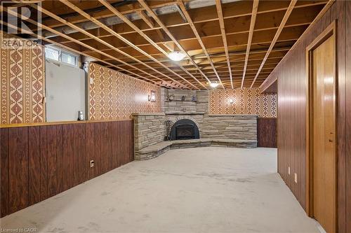 Expansive room featuring a stone-faced fireplace with a built-in hearth, exposed ceiling joists, and a combination of wood-look paneling and patterned wallpaper on the walls - 1862 Briarwood Drive, Cambridge, ON - Indoor