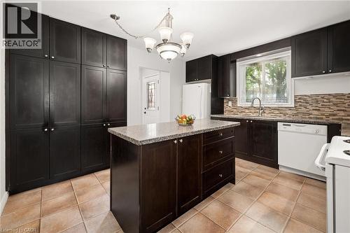 Kitchen featuring dark wood cabinetry, a central island with a light-toned countertop, and a mosaic tile backsplash - 1862 Briarwood Drive, Cambridge, ON - Indoor Photo Showing Kitchen