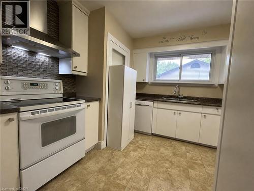 Kitchen featuring a mosaic tile backsplash, stainless steel range hood, ample white cabinetry, dark countertops, and resilient flooring - 917 Orpha Street, Burlington, ON - Indoor Photo Showing Kitchen With Double Sink