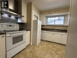 Kitchen featuring a mosaic tile backsplash, stainless steel range hood, ample white cabinetry, dark countertops, and resilient flooring - 