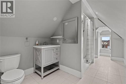 Bathroom featuring sloped ceilings, a single vanity with a solid surface countertop, a wall-mounted mirror, white ceramic tile flooring, and a shower with a white tile surround - 181 West Avenue N Unit# 4, Hamilton, ON - Indoor Photo Showing Bathroom