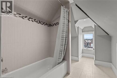 Attic bathroom featuring a full bathtub with tiled surround, decorative mosaic tile accent, sloped ceiling, and a window providing natural illumination - 181 West Avenue N Unit# 4, Hamilton, ON - Indoor Photo Showing Bathroom
