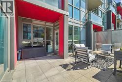 Expansive outdoor patio featuring light-toned large format tile flooring, a vibrant red overhang, glass paneled privacy screens, and floor-to-ceiling windows - 