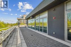 Expansive outdoor terrace featuring paver stone flooring, a modern glass and metal railing system, and multiple glass door entries - 