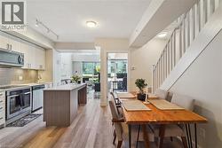 Contemporary kitchen featuring light wood-finish flooring, stainless steel appliances, a center island with countertop seating, and light-toned cabinetry - 