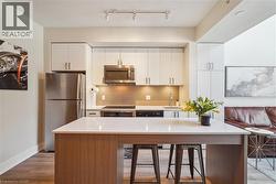 Modern kitchen featuring a large island with white countertop, stainless steel appliances, white cabinetry, a tiled backsplash, and recessed lighting - 